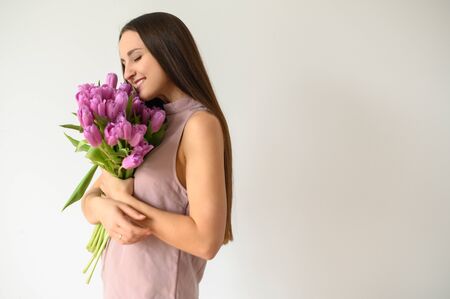 Spring mood. Young attractive woman in casual wear with a bouquet of bright tulips. Picture on a white background with empty space.の写真素材
