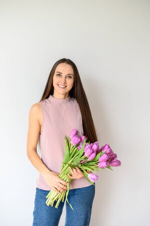 Young attractive girl with fresh flowers tulips. Spring mood, colorfull and pastel colors. Indoor image on a white backgroundの写真素材