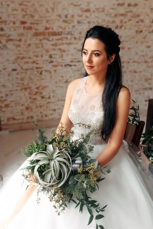 A charming and tender image of a bride with a bouquet of herbs and green branches in the style of boho, rustic. Studio photo with natural lightの写真素材