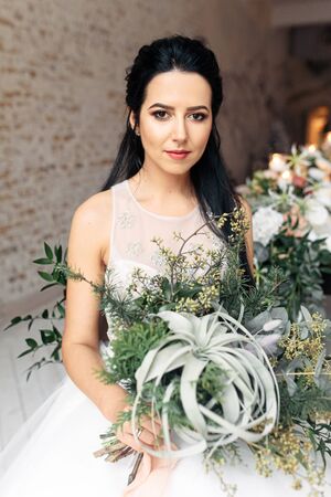 Boho style wedding. Beautiful bride in a chic dress with a nontrivial wedding bouquet without flowers. She is looking at the camera with a serious face.の写真素材