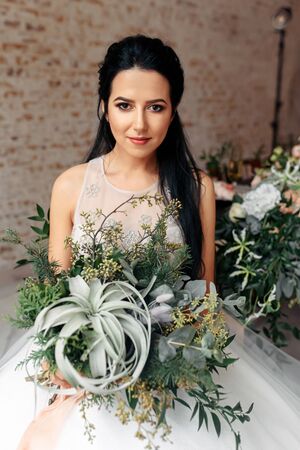 Boho style wedding. Beautiful bride in a chic dress with a nontrivial wedding bouquet without flowers. She is looking at the camera with a serious face.の写真素材