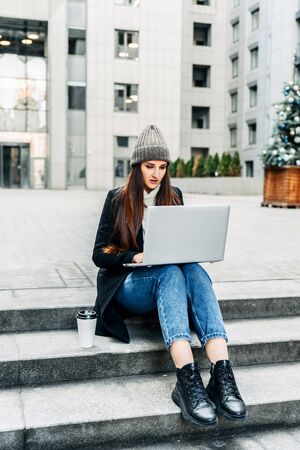 The work of a freelancer. Woman freelancer uses a laptop, she sits on the steps in the business centerの写真素材