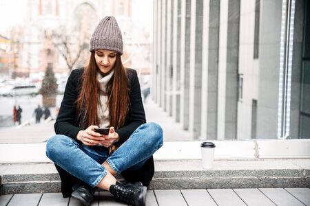 Life on social networks. Young woman chatting, typing something on the phone in the urban landscape outdoorsの写真素材