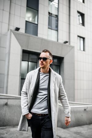 Male fashion model. Handsome young man in a stylish coat and sunglasses in an urban landscapeの写真素材