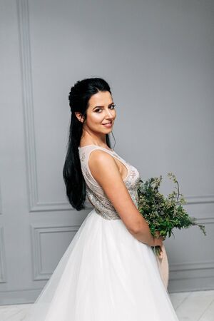Studio photo of a bride with a natural professional make-up and with a green bouquet in her hands. View from the backの写真素材