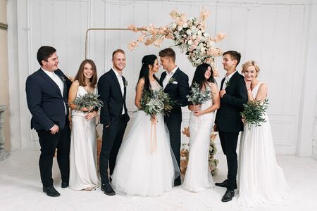 Stylish group photo at the wedding. Newlyweds, bridesmaids and best men stand in a row near the wedding archの写真素材