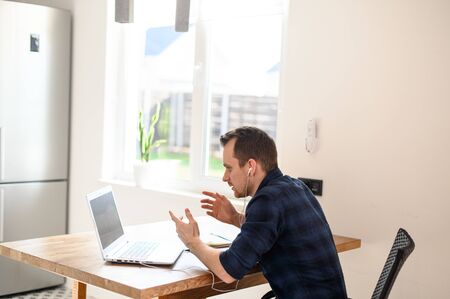 An office employee works from home. Video call meeting, online conference. A young guy sits in front of a laptop, talking and gesturingの写真素材