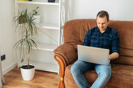Work remotely, work at home. Young positive man sits on a sofa with a laptopの写真素材