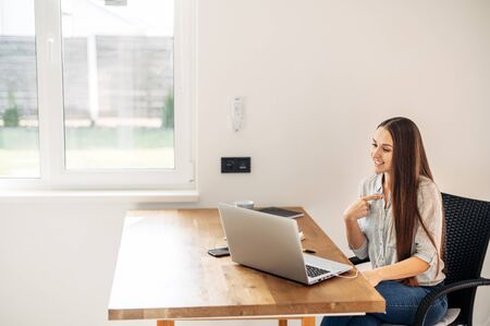 An office employee works from home. Video call meeting, online conference. A young woman sits in front of a laptop, talking and gesturingの写真素材
