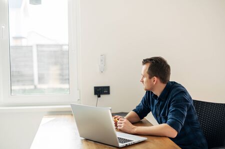 The guy uses a laptop to work at home. He is thoughtful and looks out the window.の写真素材