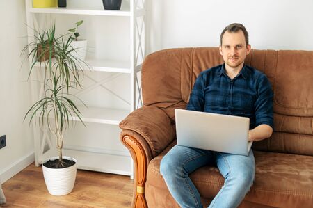 Work remotely. Work in a relaxed rhythm. Young guy working on a laptop while sitting on a sofa at homeの写真素材