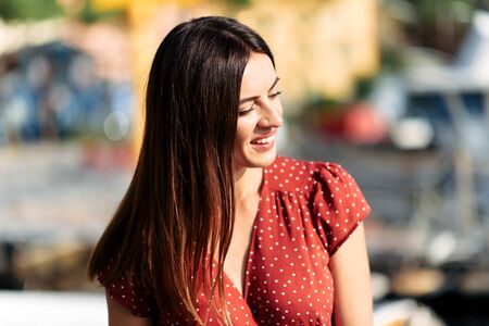 Portrait of a beautiful young brunette woman in a red dress in natural sunlight. She smiles