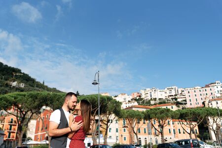 Love story in Italy. A couple in love are standing in an embrace, a beautiful girl in a dress and an attractive guy in a vest. View of the colorful houses in the Mediterranean style in the backgroundの写真素材