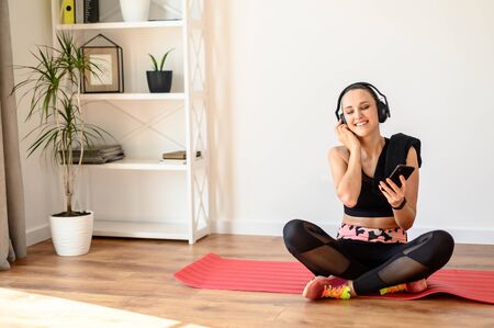 Music for fitness. A young woman listens to her favorite music in wireless headphones during sports at home, she closed her eyes from pleasure.の写真素材
