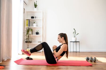 Stay home. Sports activities at home during quarantine. Young slim woman in sportswear doing fitness exercises on mat at homeの写真素材
