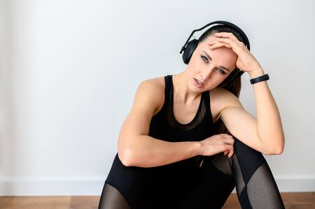 Sport lifestyle, sport fashion. Attractive young girl in a black sports outfit and in headphones looks at the camera with a serious face. Close-up portrait, gorizontal picture on white backgroundの写真素材