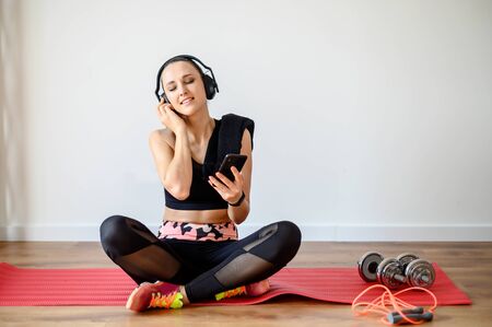 Music for fitness. A young woman listens to her favorite music in wireless headphones during sports, she closed her eyes from pleasure.の写真素材