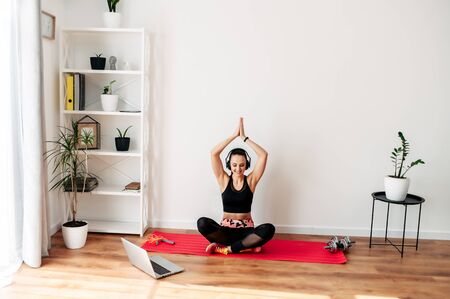The concept of online training, sports video lessons. Young slim athletic girl practices yoga at home in online lessons. Laptop in front of herの写真素材