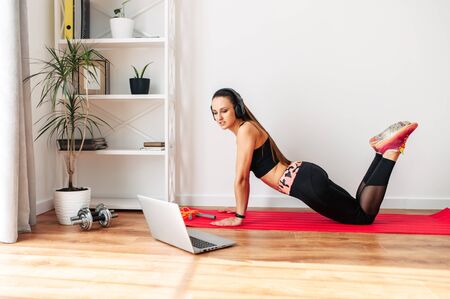 Stay home. The young woman is doing fitness, sports exercises at home during quarantine. She is watching a fitness video tutorial on a laptop.の写真素材