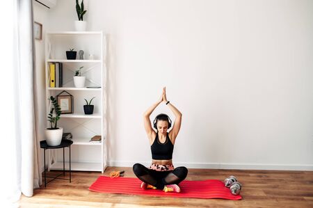 The concept of a healthy lifestyle, sports at home. A girl on a rug in a sportswear practices yoga, she listens to music in headphonesの写真素材