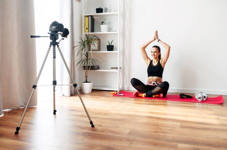 Video training, online master class. A young woman practicing yoga at home and recording video tutorial on cameraの写真素材