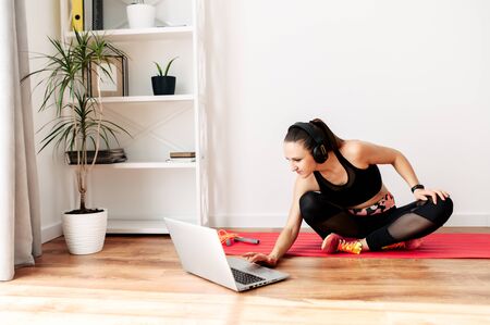 Stay home. The young woman is doing fitness, sports exercises at home during quarantine. She is watching a fitness video tutorial on a laptop.の写真素材