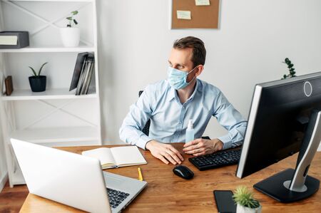 Work from home in the midst of a coronavirus pandemic, Covid 19, seasonal flu. A young man uses a medical mask and a hand sanitizer to protect himself. He works on a laptop. Stay at homeの写真素材
