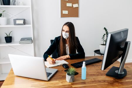 Stay at home, office at home, work remotely. Woman in medical mask writes recommendations in a notebook with penの写真素材