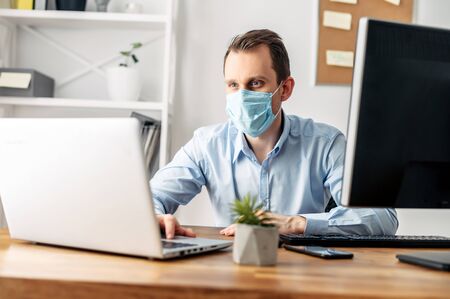 Viral threat, seasonal viral diseases. A man works in the office in a medical mask, protecting office workers from virusesの写真素材