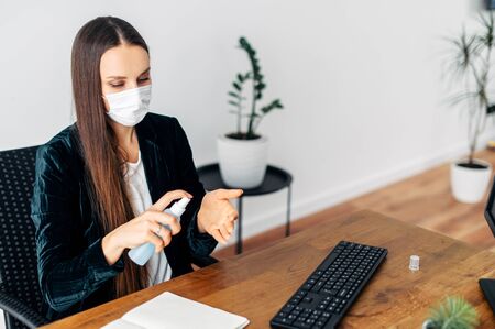 Stay at home. A young woman works from home using a computer and laptop. A woman in a medical mask carefully treats her hands with an antisepticの写真素材