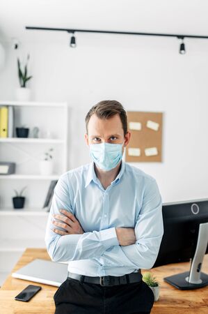 Protect yourself during a viral pandemic. A man in a smart casual shirt and medical mask is standing with his arms crossed on his chest. Office at home, office styleの写真素材
