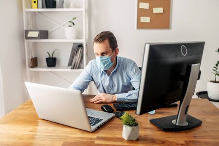 Coronavirus pandemic, covid 19. Office worker man working with a laptop in a medical mask. Virus protectionの写真素材