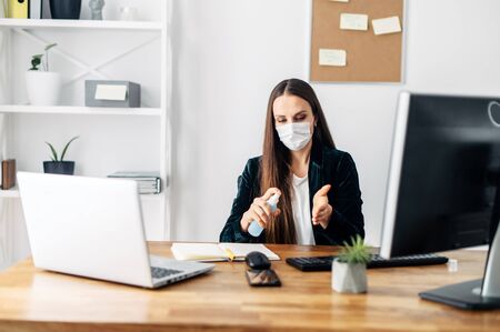 Stay at home. A young woman works from home using a computer and laptop. A woman in a medical mask carefully treats her hands with an antisepticの写真素材