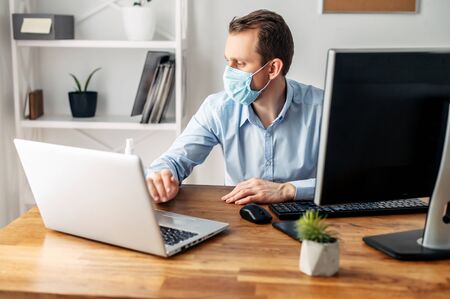 Coronavirus pandemic, covid 19. Office worker man working with a laptop in a medical mask. Virus protectionの写真素材