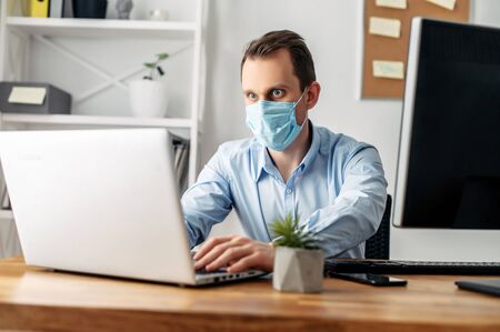 Viral threat, seasonal viral diseases. A man works in the office in a medical mask, protecting office workers from virusesの写真素材