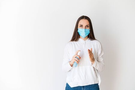 Protect yourself from viruses, covid, coronavirus. A woman in casual clothes in a medical mask sprays a disinfectant, a sanitizer in the palm of her hand. Isolated on white backgroundの写真素材