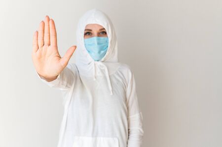 Quarantine, pandemic, cove. A woman in a protective suit and medical mask holds her hand in front of her with an open palm indicating the stop sign.の写真素材