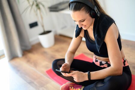 Get in shape yourself. A young woman in sport look is training at home, she takes a break between sets and chatting on the phone. Concept of healthlife, sportの写真素材