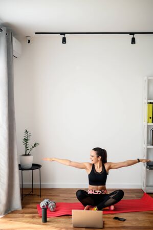 Online training, online video tutorial. A young woman in sportswear is using a laptop to watching workout video tutorial at home. She lying on the mat, looks at the screen and repeats the exercises.の写真素材