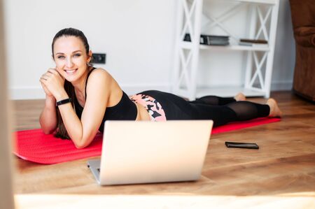 Online training, online video tutorial. A young woman in sportswear is using a laptop to watching workout video tutorial at home.の写真素材