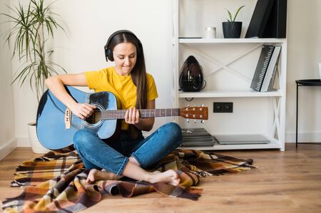 Stay home. A young woman spends her leisure time at home playing music. She is sitting on a cozy plaid with an acoustic guitar in her hands.の写真素材