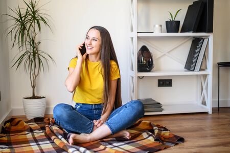 Stay at home. Home leisure during quarantine, epidemic. A young woman speaks on the phone and laughs, she sits on a cozy plaidの写真素材