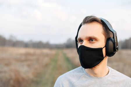 Close Up portrait of a guy in headphones and in black medical mask outdoors. Concept active and...