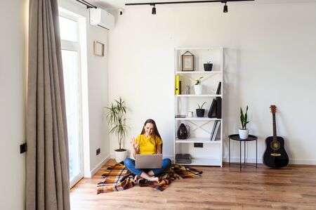 Freelancer woman works from home, work remotely. Young woman in casual clothes sitting with a laptop on a cozy plaid in a stylish minimalistic interior.の写真素材