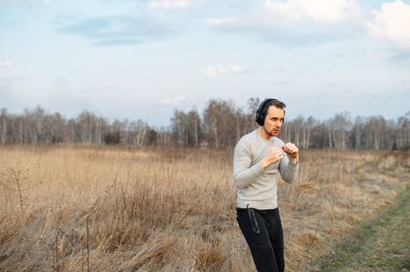 Get in shape. A young guy in headphones is doing sports training in the open air in the spring. He is warming up and boxing.の写真素材