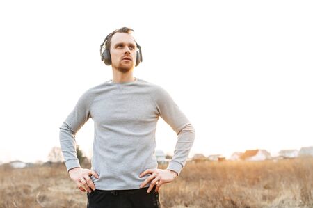 Successful athletic guy in headphones stands in a field on country side in sunset light. Outdoor workout. Concept of healthy lifestyle, outdoor trainingの写真素材