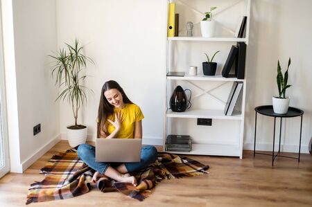 Video communication, zoom. Young positive woman in a yellow casual t-shirt communicates via video communication using a laptop at homeの写真素材
