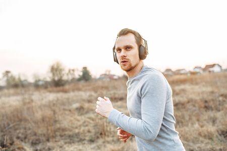 Training outside the city in the open air. Young attractive athletic man jogging in a meadow in sunset light. The concept of self-discipline and a healthy lifestyle. Photo in motionの写真素材
