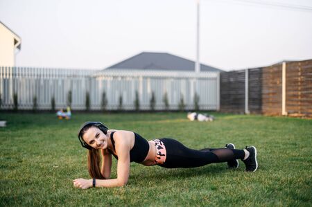Concept of a healthy lifestyle, self-discipline. A young girl in sportswear does an exercise plank on the grass outdoorsの写真素材