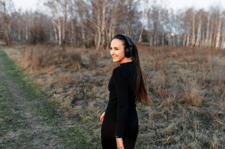 Young attractive athletic woman in black sports outfit and headphones in the countryside. Outdoor Training Conceptの写真素材
